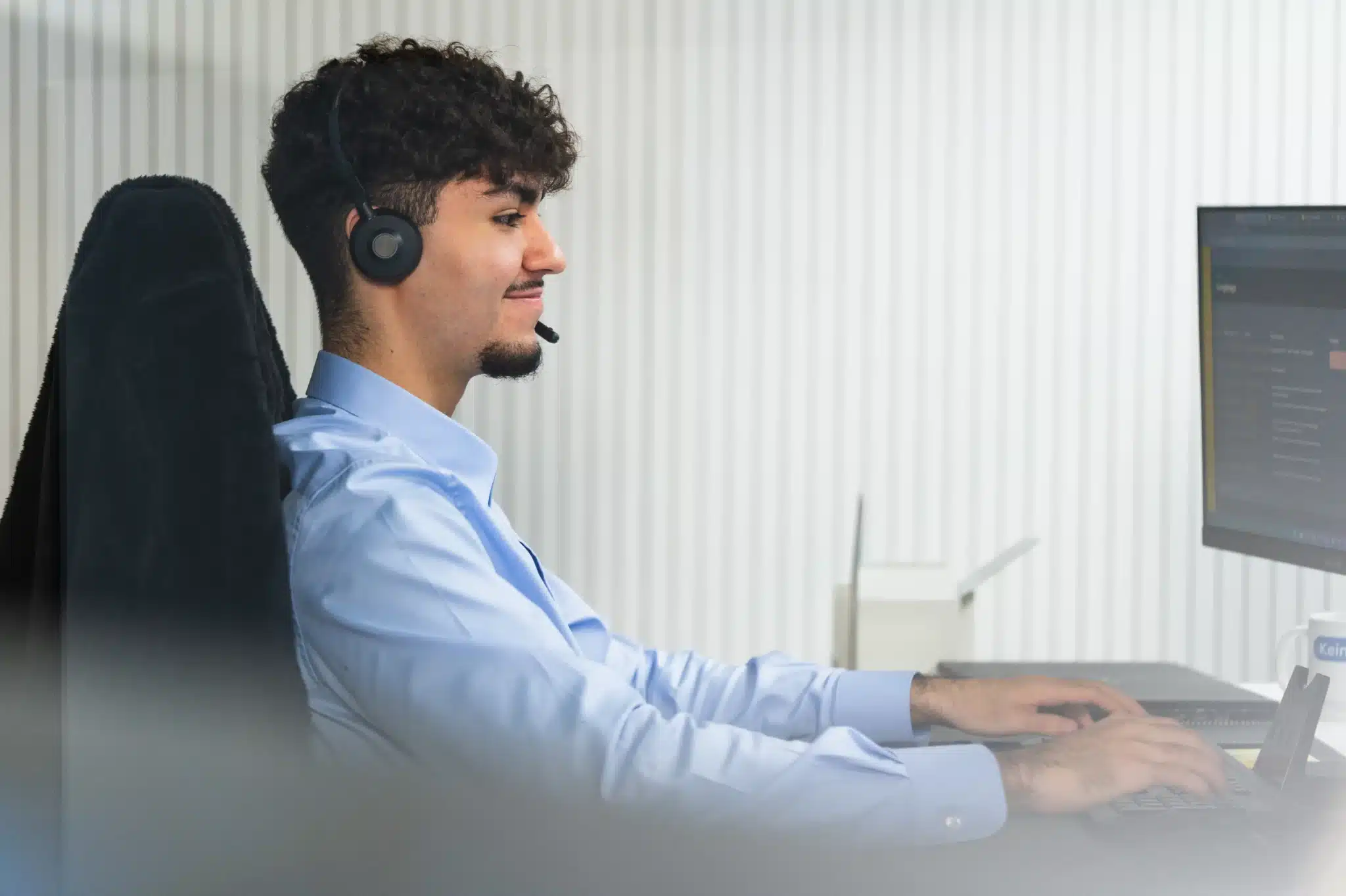 IT-Experte arbeitet lächelnd am Schreibtisch vor zwei Monitoren in einem modernen Büro